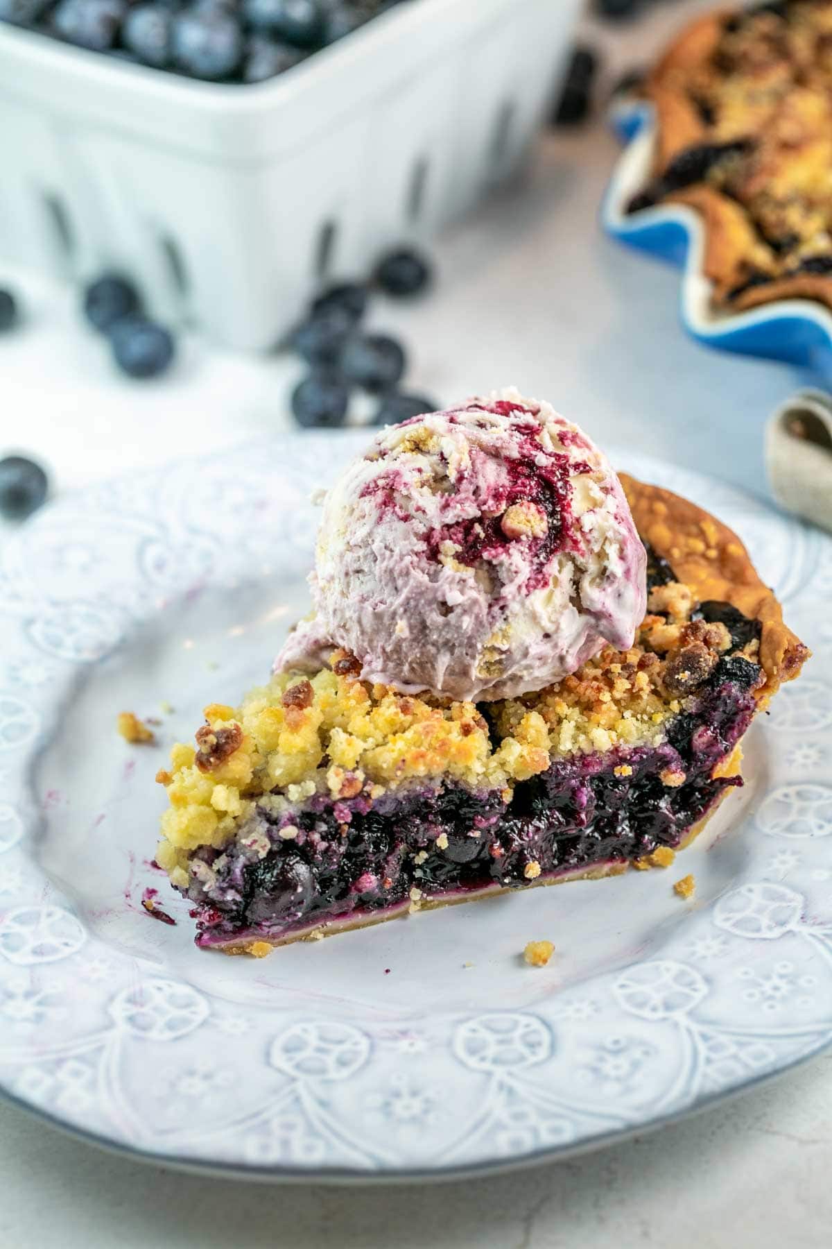 side view of a slice of blueberry pie with a scoop of ice cream on top