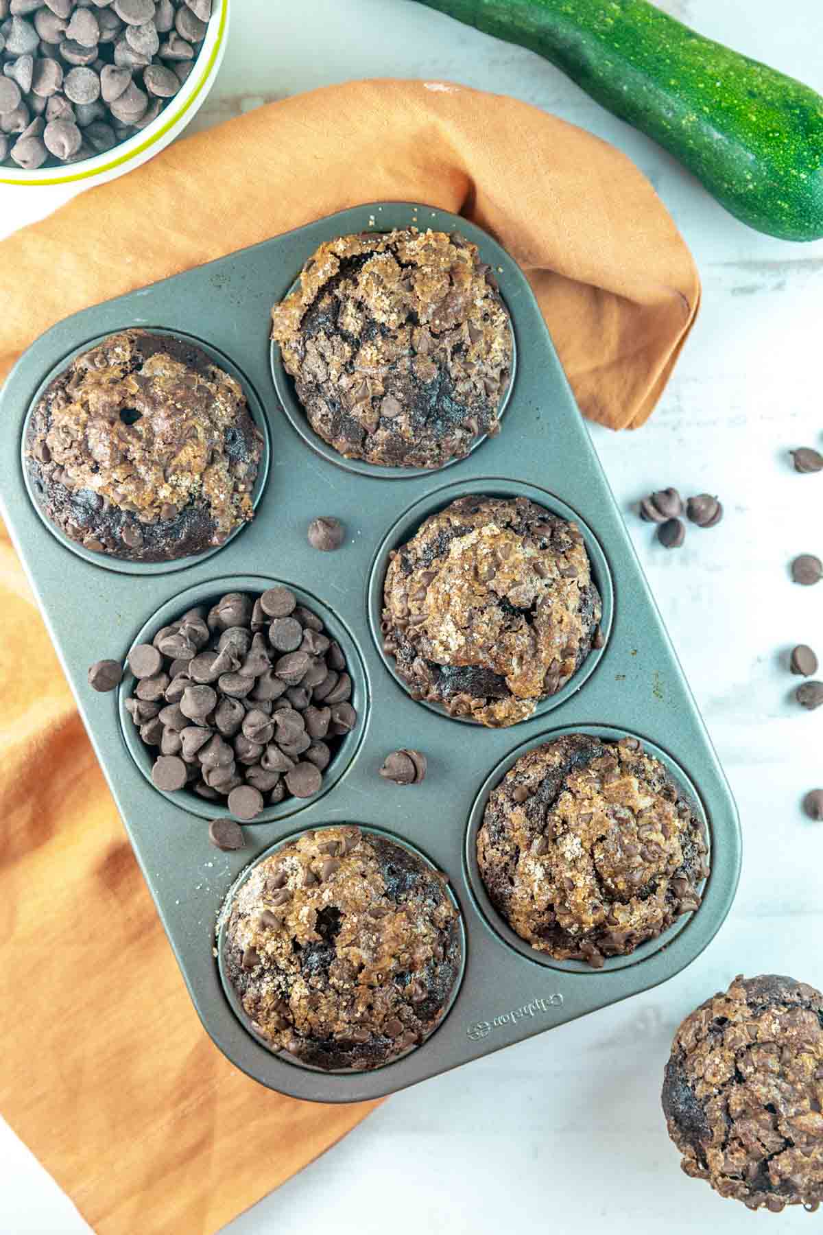 6 well muffin tin filled with 5 zucchini muffins and one well filled with chocolate chips