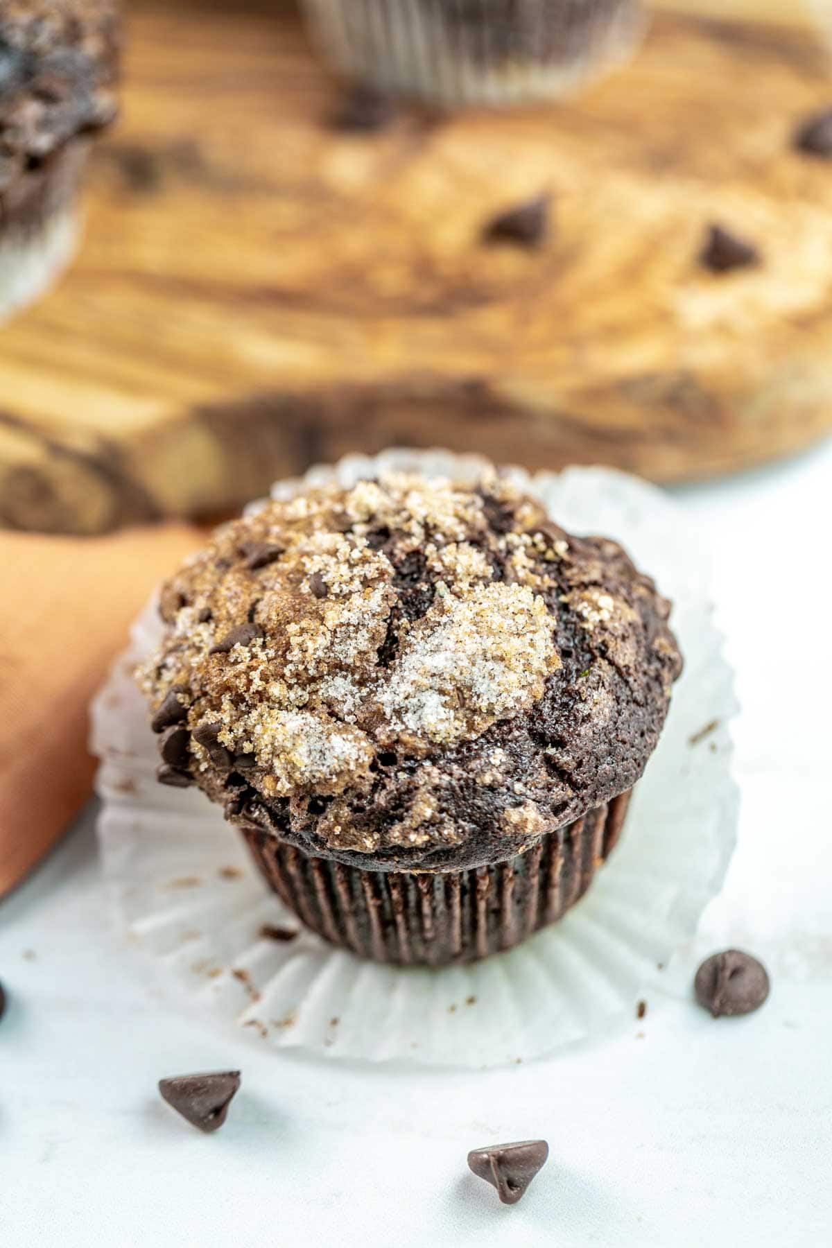 chocolate zucchini muffin with a sugar crumb topping on an unwrapped parchment paper muffin liner