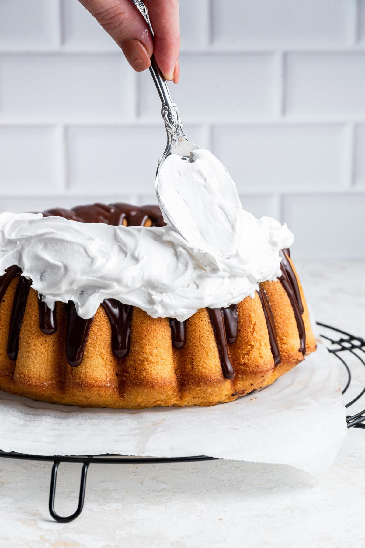 spooning marshmallow meringue buttercream onto a s'mores bundt cake