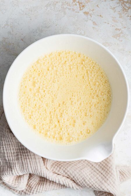 frothy mixed eggs and oil in a white mixing bowl