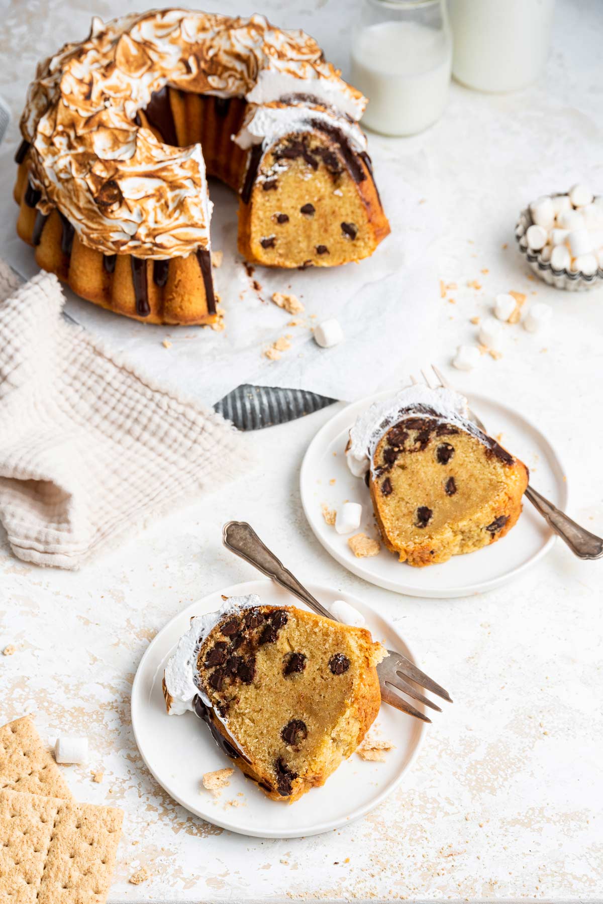 two slices of s'mores bundt cake on dessert plates with the rest of the cake visible in the background