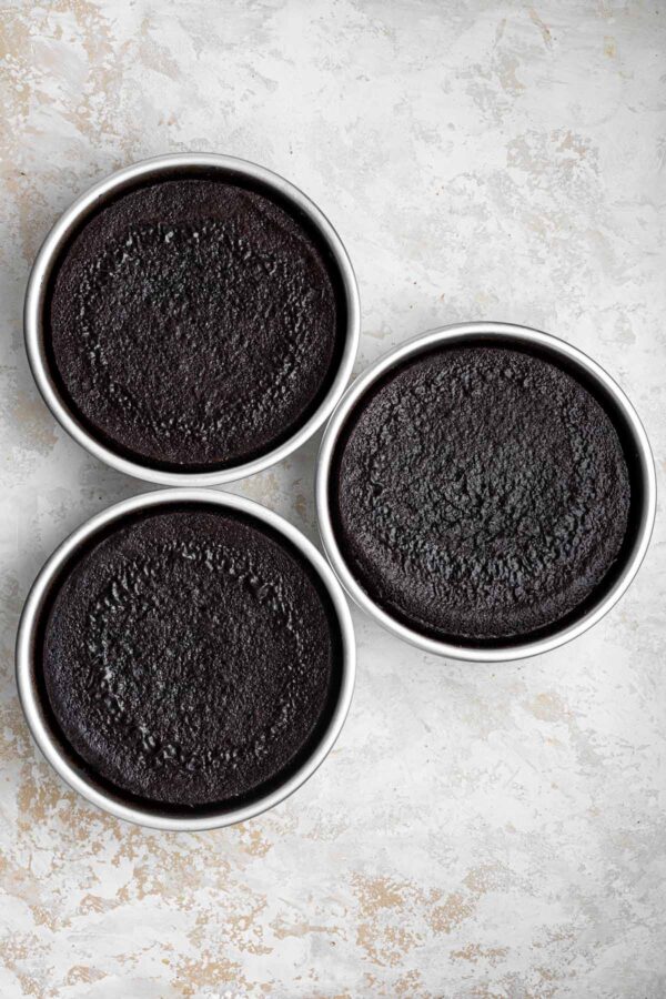 three freshly baked dark chocolate cakes still in the cake pans.