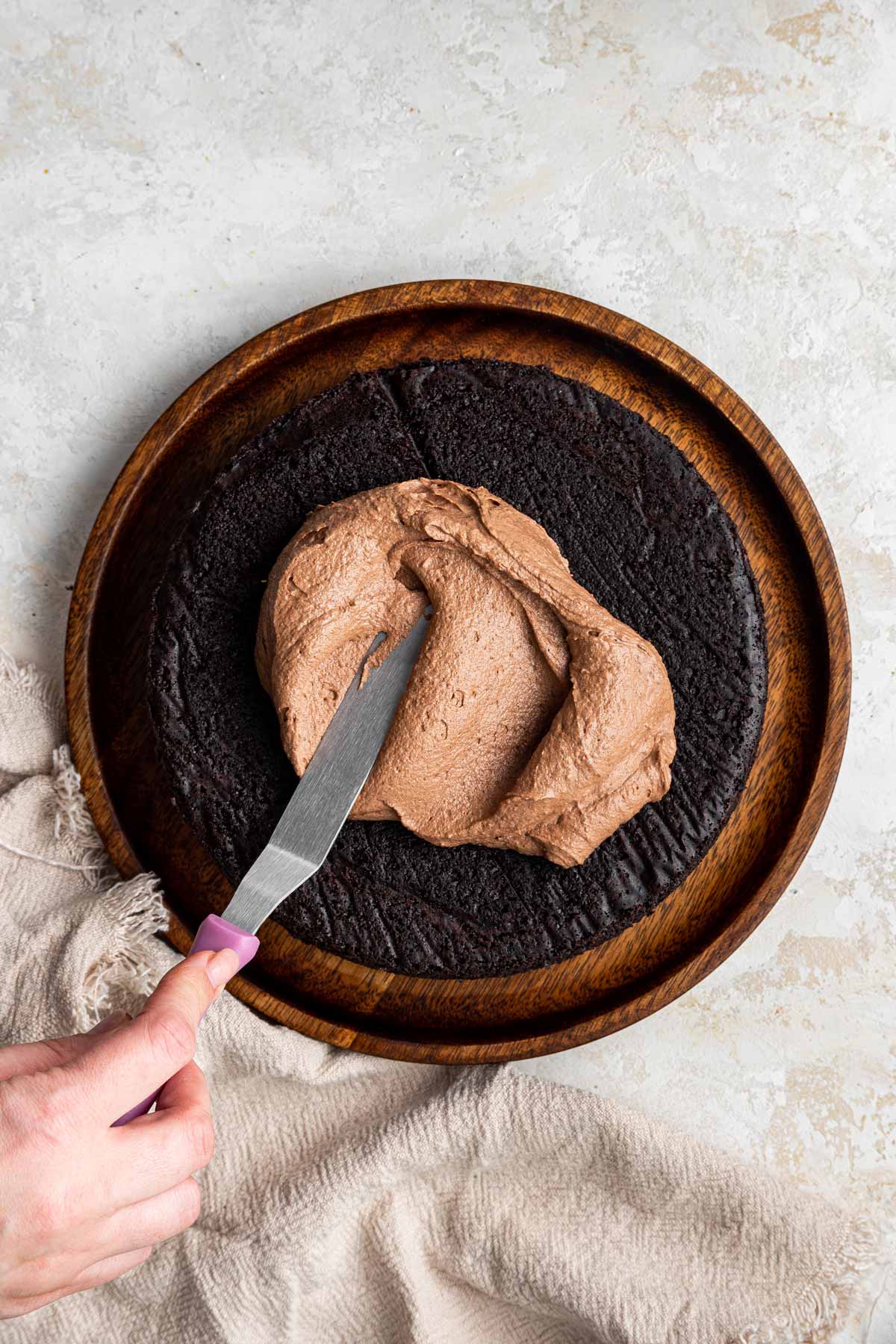 spreading frosting across the top of a round chocolate cake.