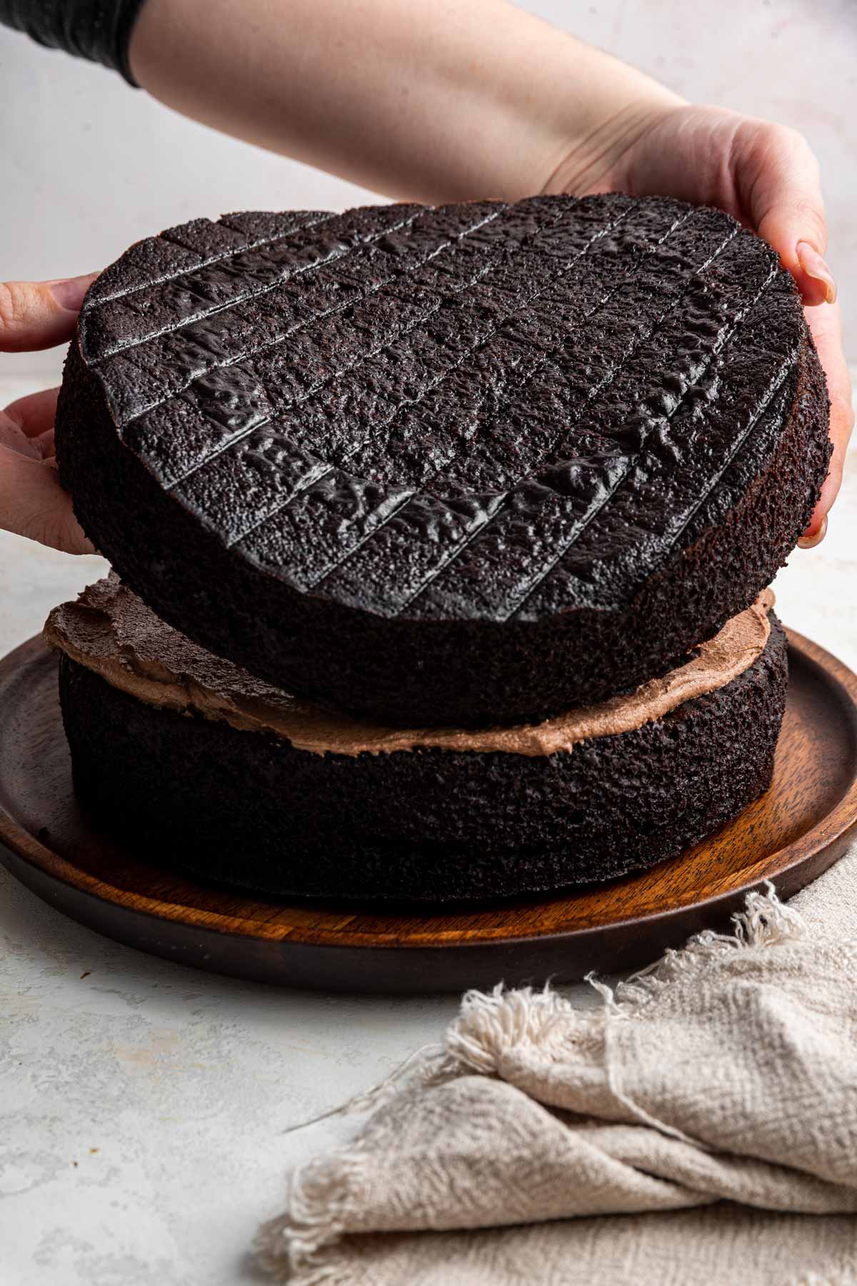 a baker placing a second layer of cake on top of one frosted layer.