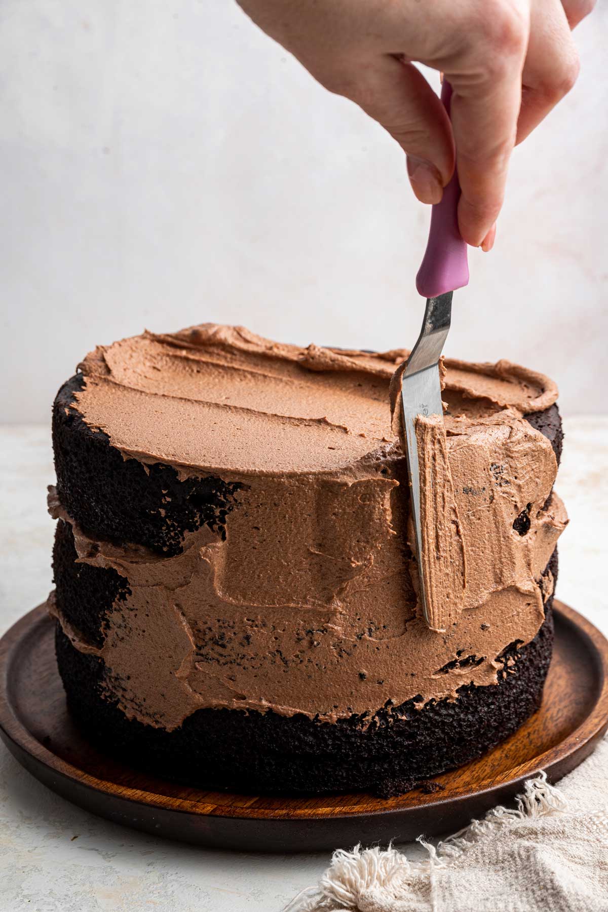 applying a thin crumb coat of chocolate frosting to a three layer cake.