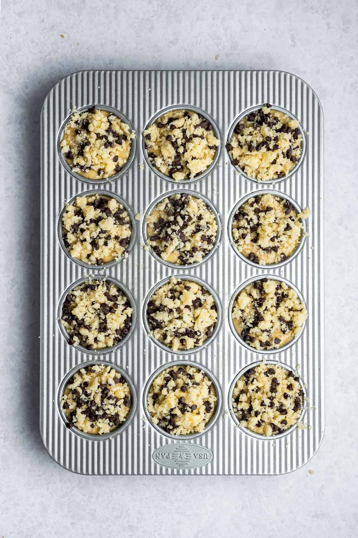 unbaked muffins in a muffin tin topped with buttery chocolate chip streusel.