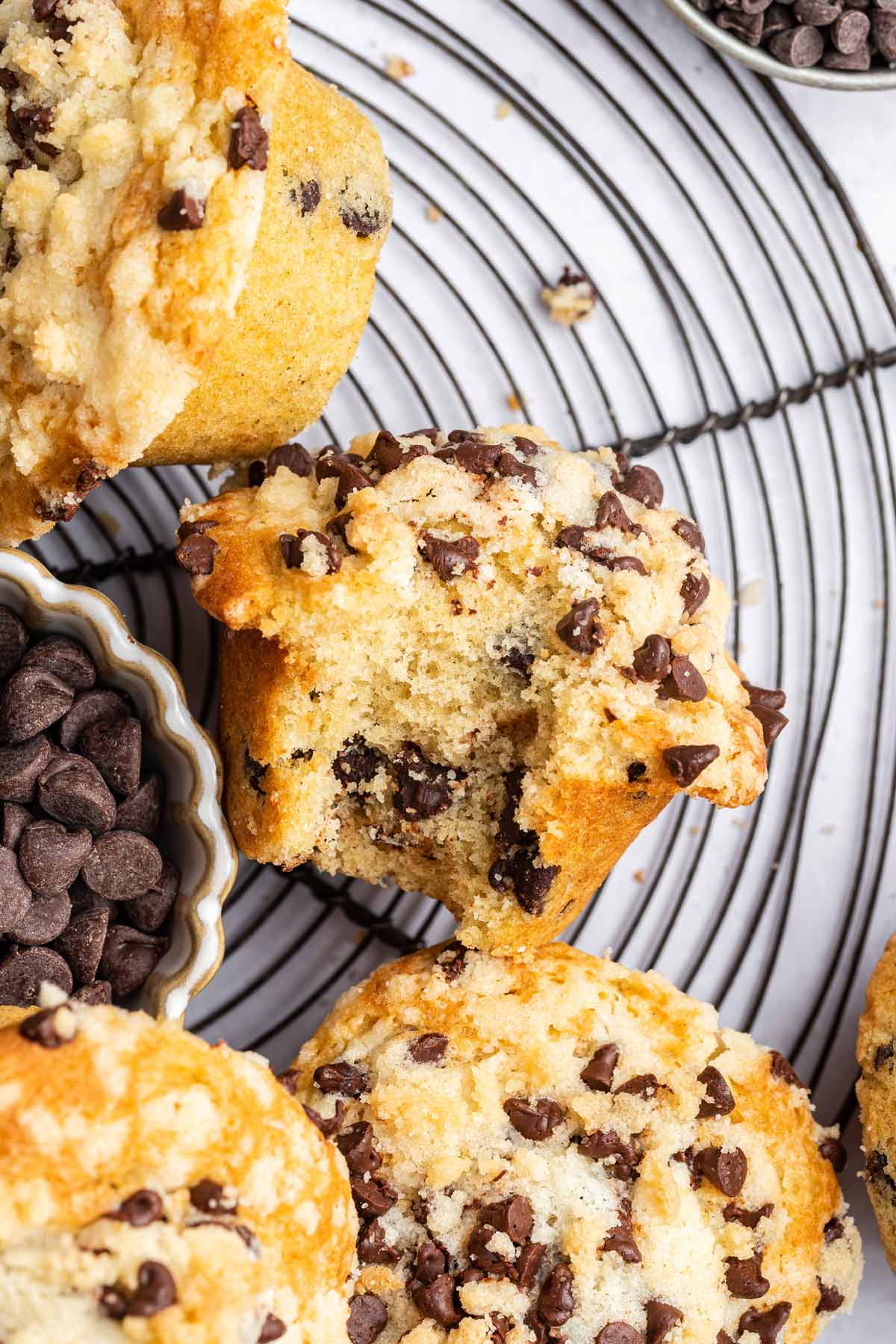 muffin with a bite taken out of it on a wire cooling rack next to a bowl of chocolate chips.