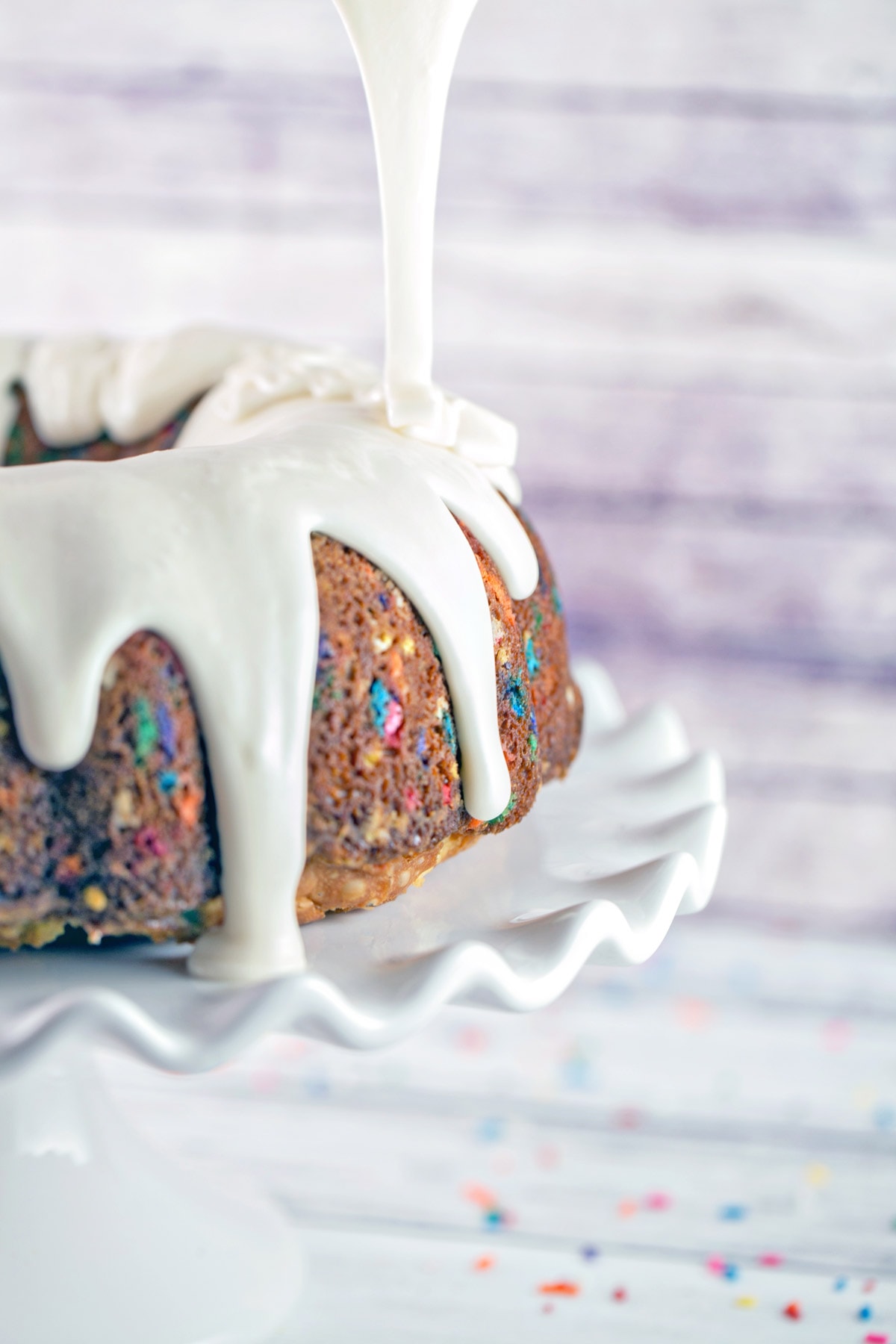 thick white glaze being poured over a bundt cake.