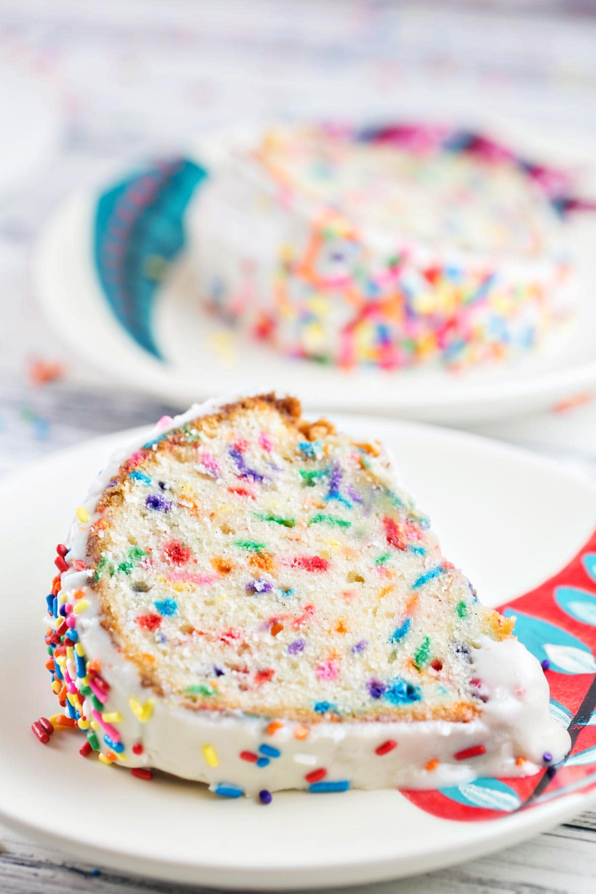 two slices of funfetti bundt cake on dessert plates covered in sprinkles.