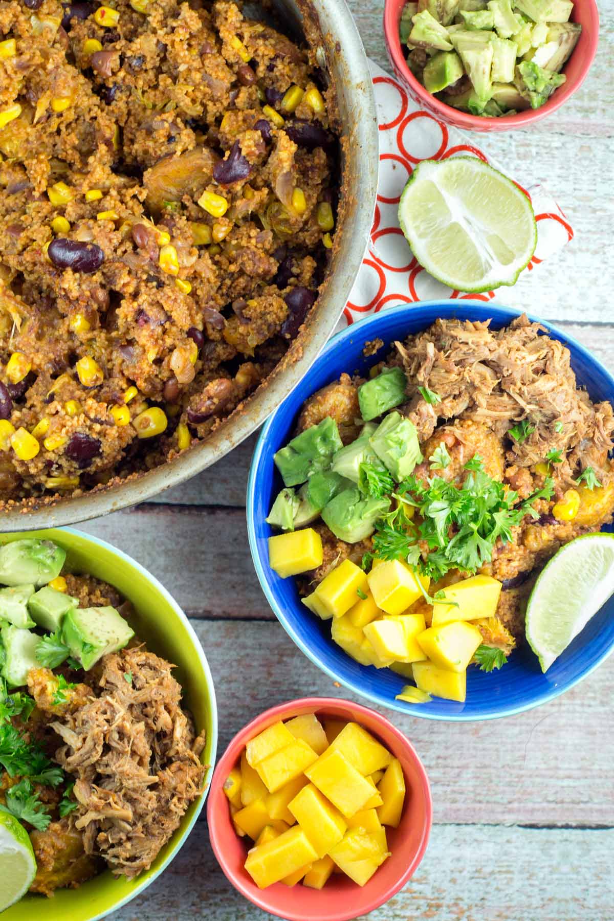 overhead view showing a couscous bowl with mango, avocado, pulled pork, and limes.