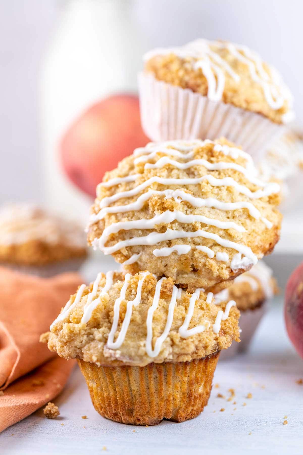 Peach muffins stacked on each other with peaches in the background. 