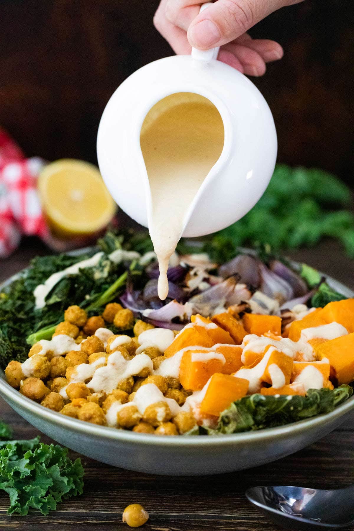 pouring maple tahini dressing onto a sweet potato chickpea bowl.