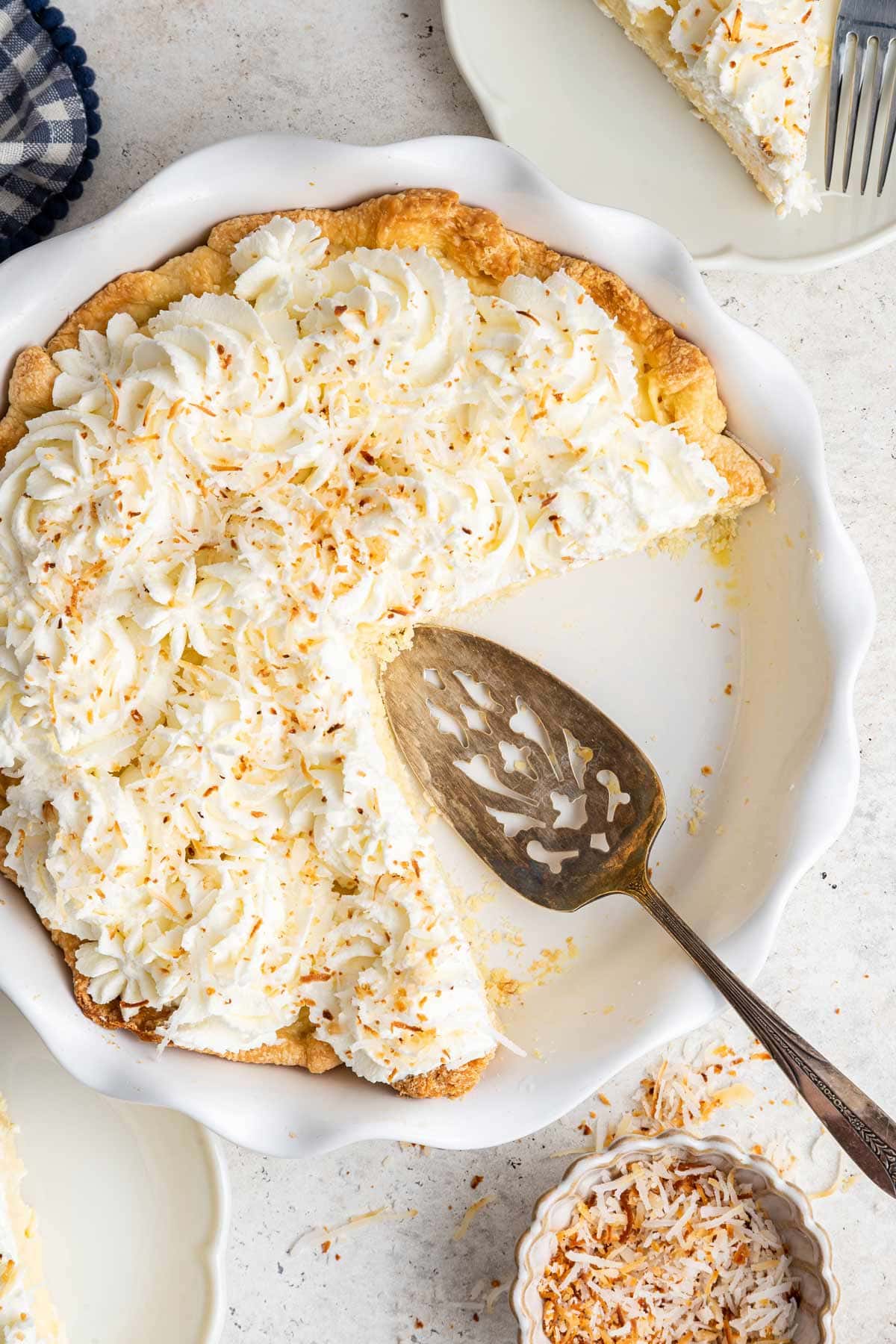 coconut cream pie in a white ceramic pie dish with two slices of pie removed.