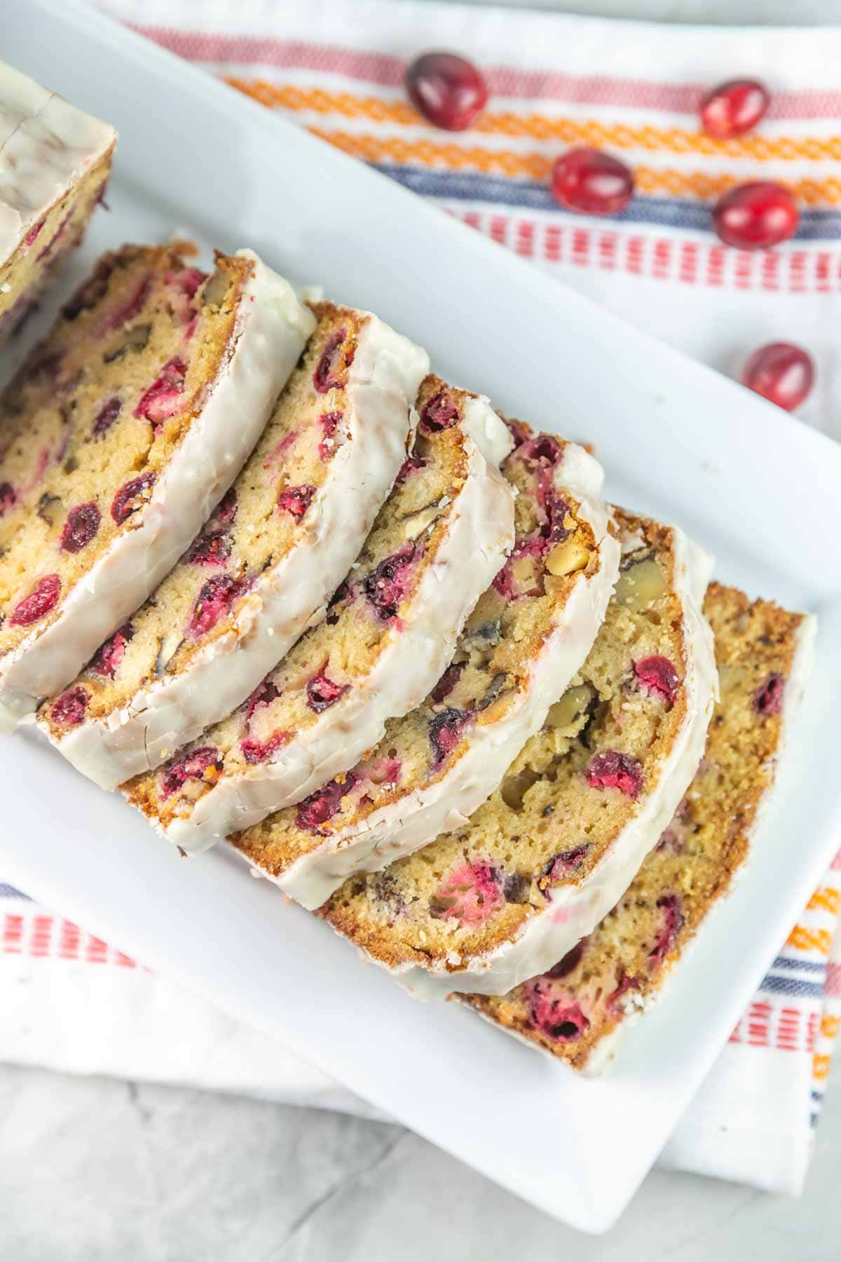 slices of cranberry bread with an opaque cider glaze arranged on a white serving dish.