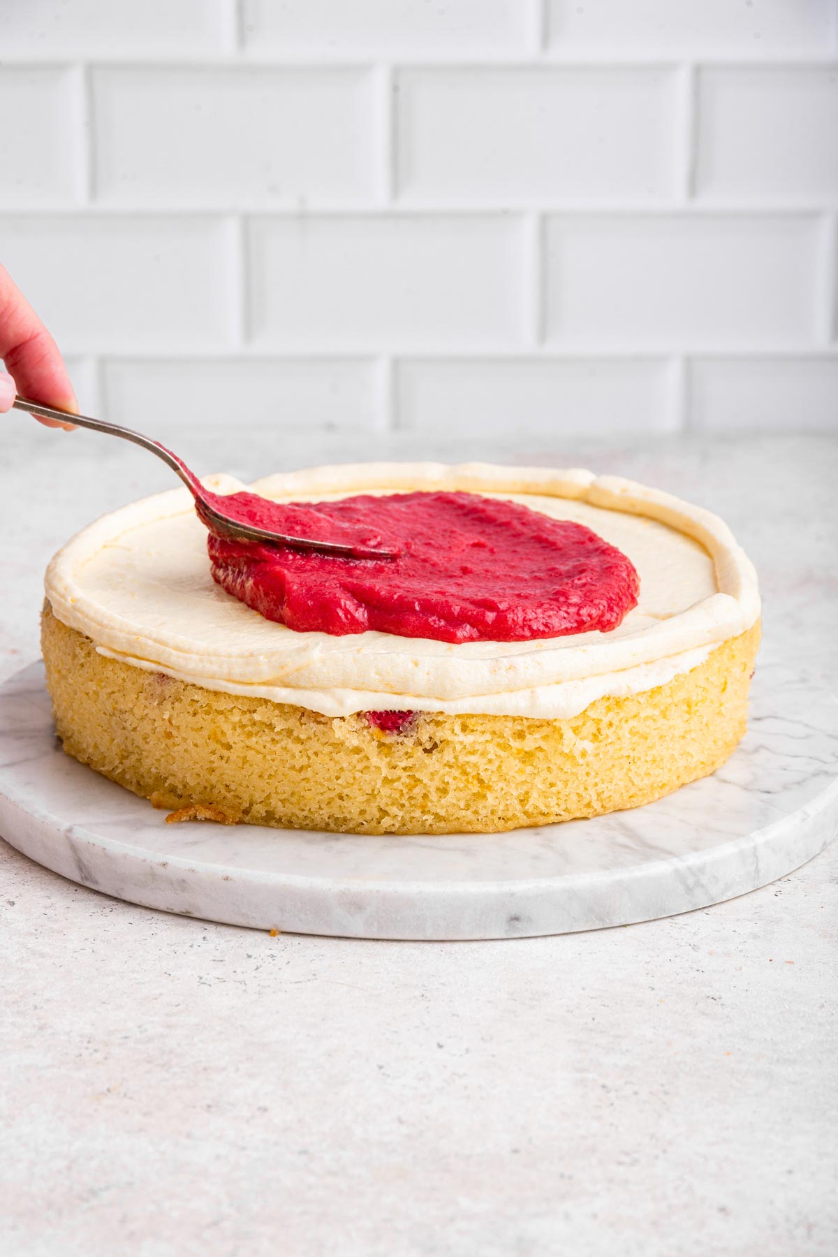 vibrant red cranberry curd being spread on a layer of cake.