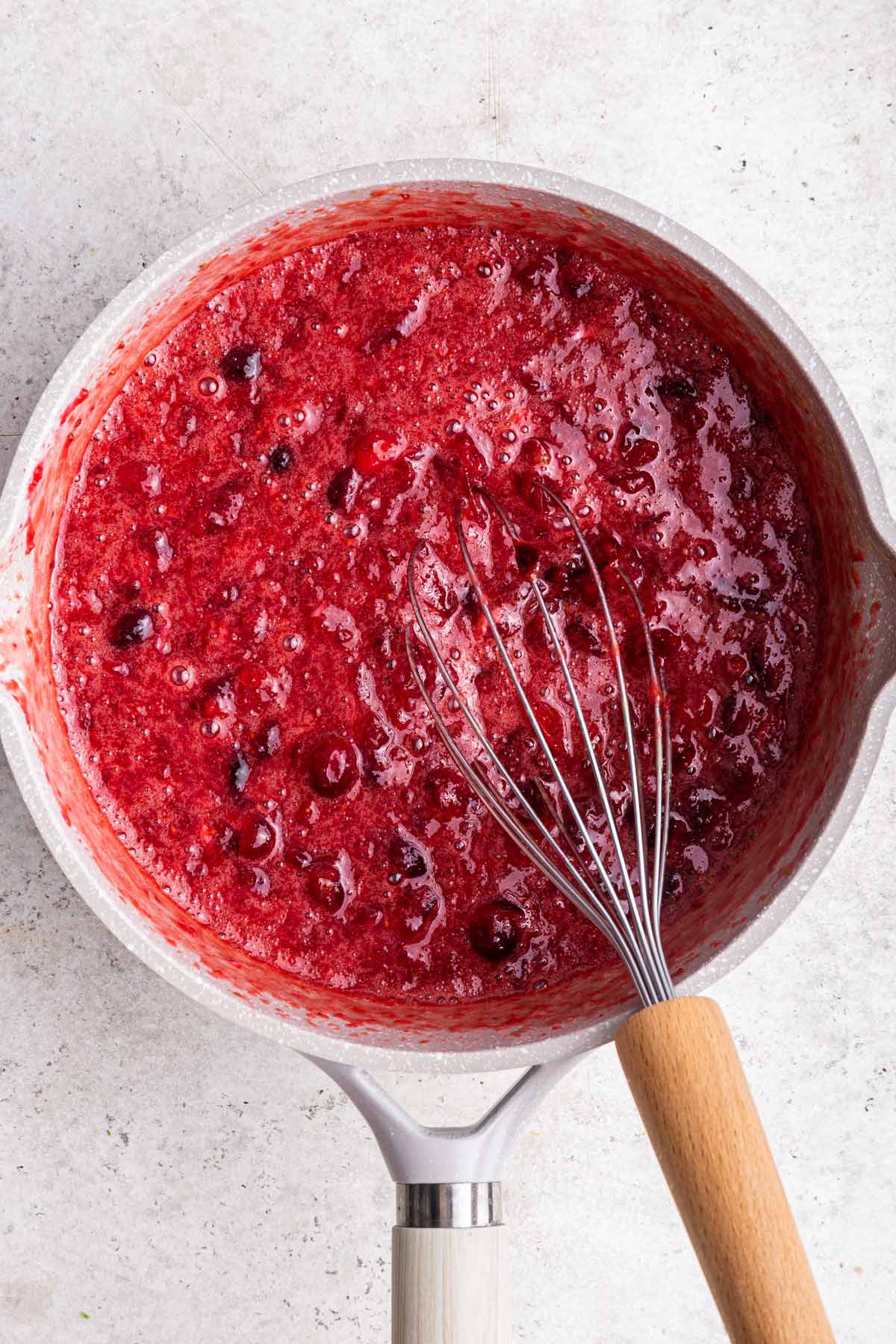 cranberry curd emulsifying into a thick solution after adding egg yolks.