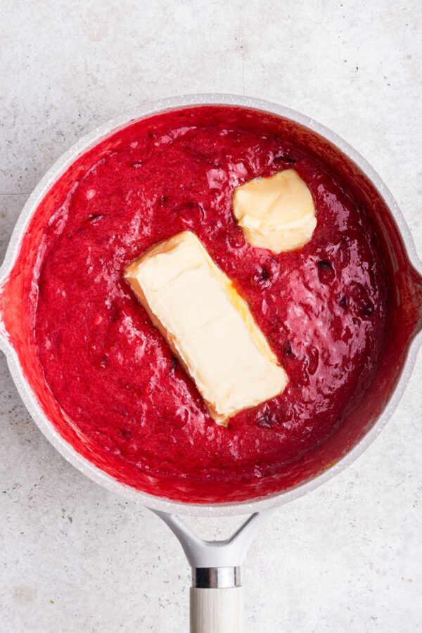 adding butter to cranberry curd in a saucepan.