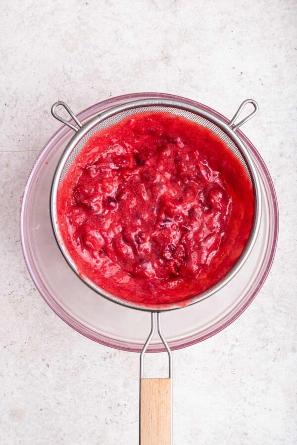 cranberry curd in a mesh strainer set over a bowl.