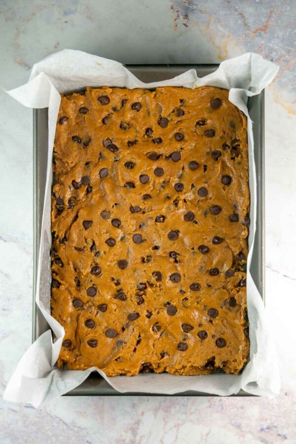 unbaked pumpkin cookie bar dough in a parchment lined baking pan