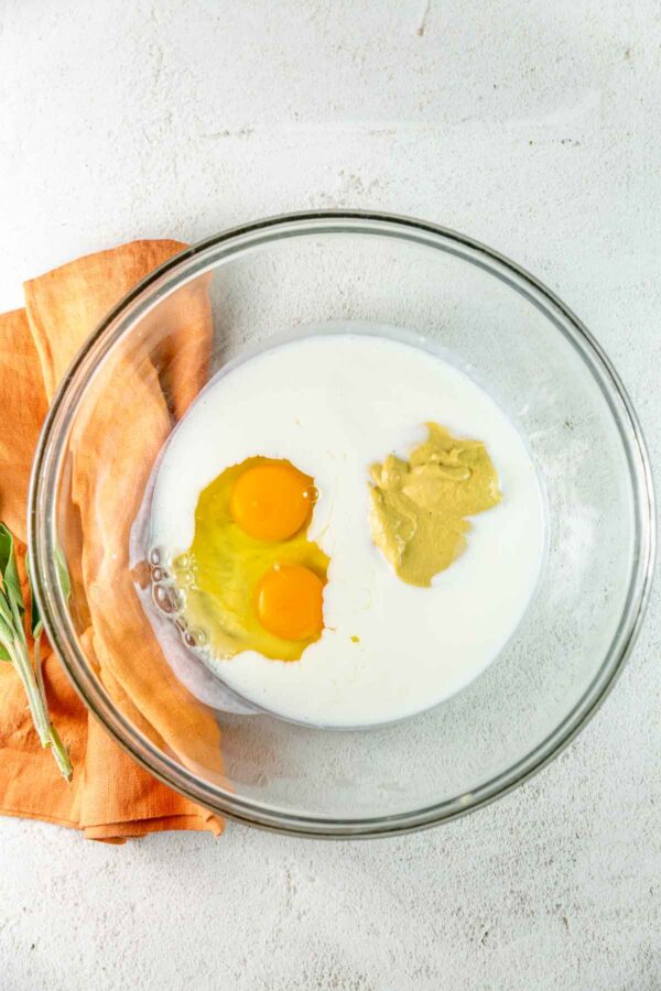 mixing bowl filed with eggs, milk, oil, and mustard.