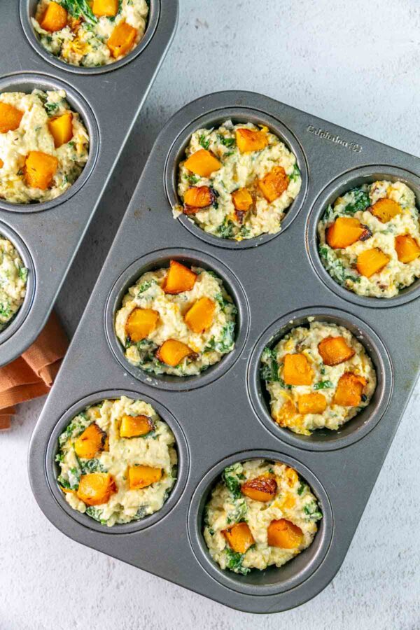 butternut squash muffin batter in muffin tins with extra squash set on top.