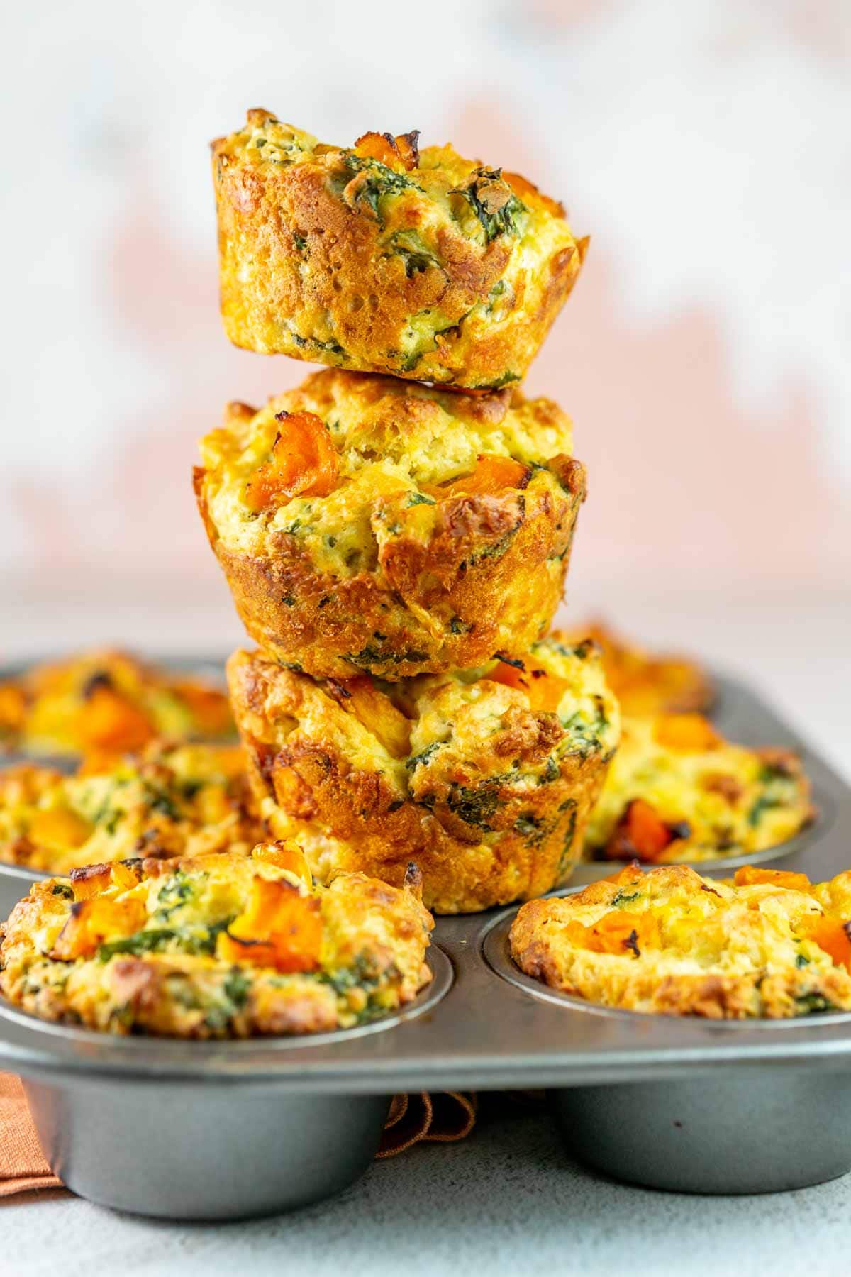 stack of three butternut squash and kale muffins on top of a muffin tin.