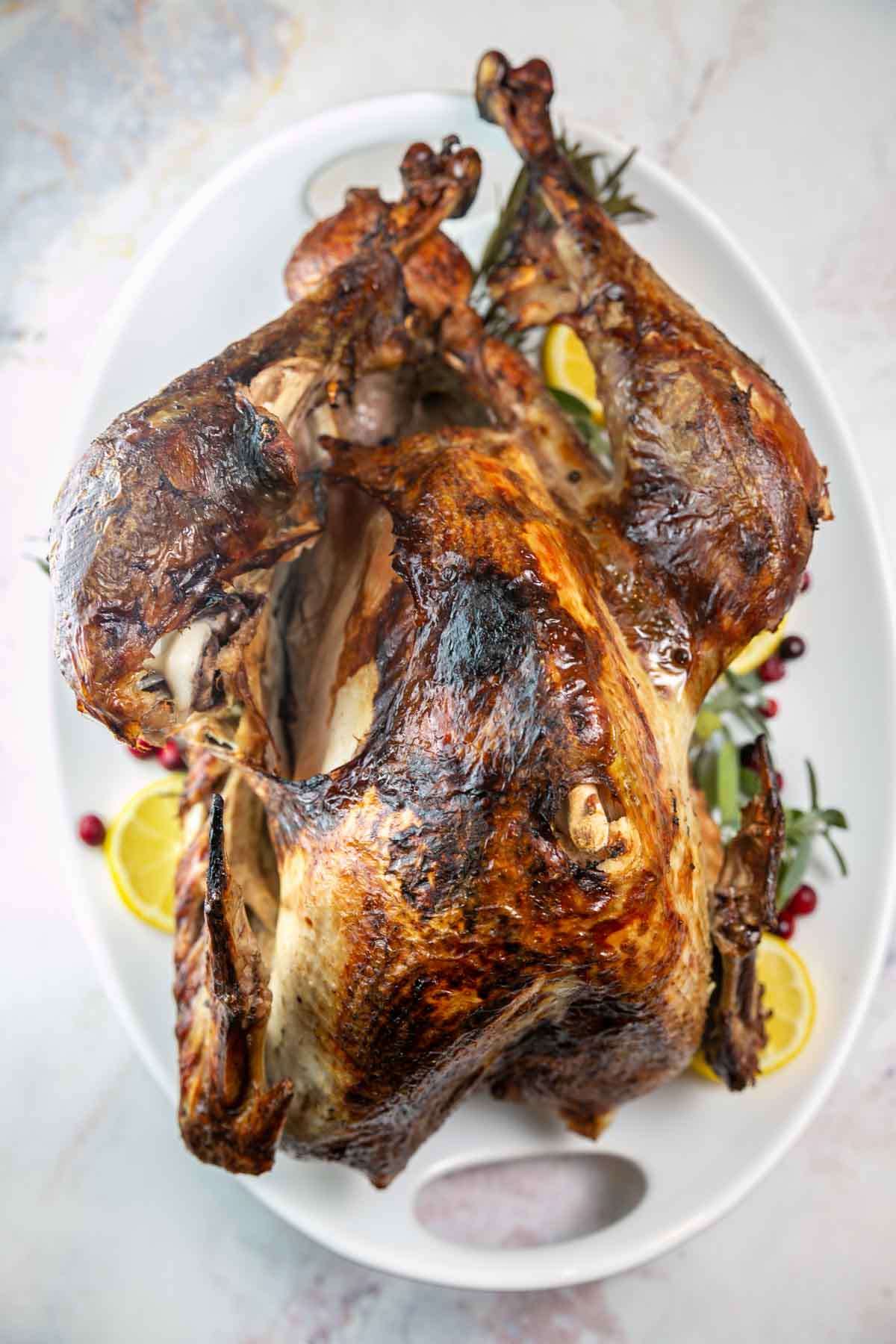 Whole roasted turkey on a serving plate with herbs, cranberries and lemons.