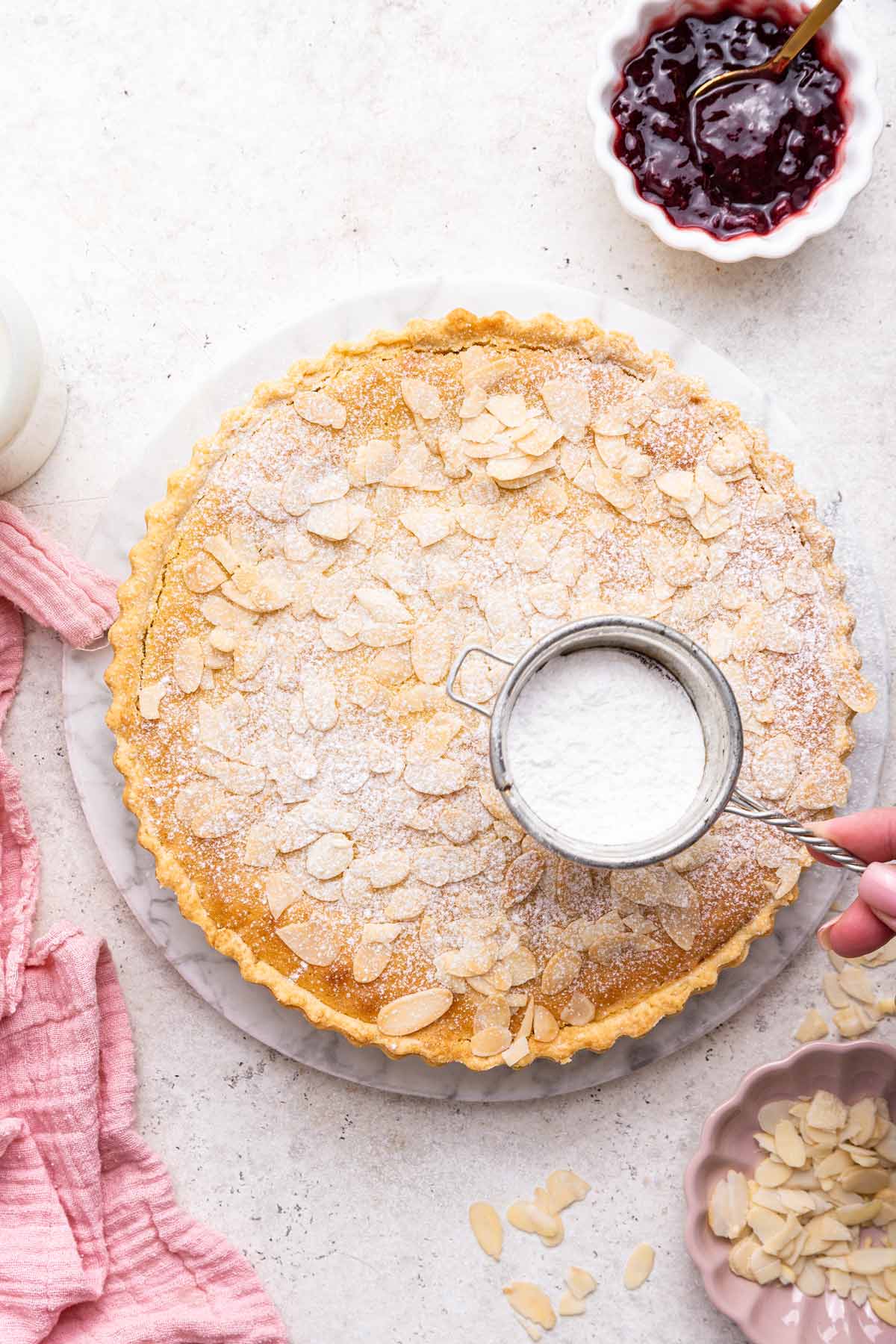 powdered sugar sifter dusting the top of a bakewell tart with a layer of sugar.