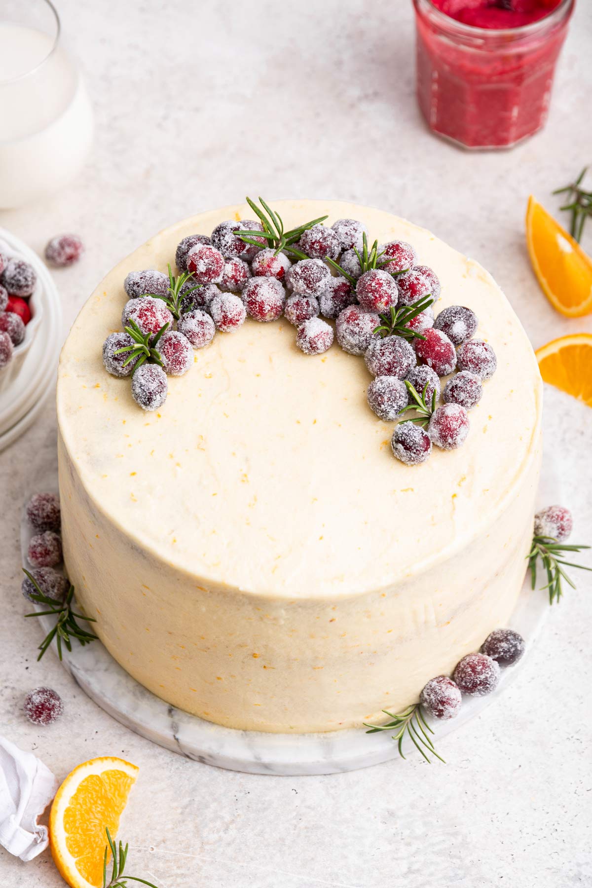 cranberry orange cake decorated with sugared cranberries and sprigs of rosemary.