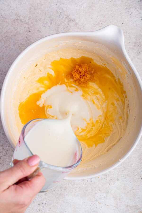 pouring buttermilk into a mixing bowl filled with cake batter.