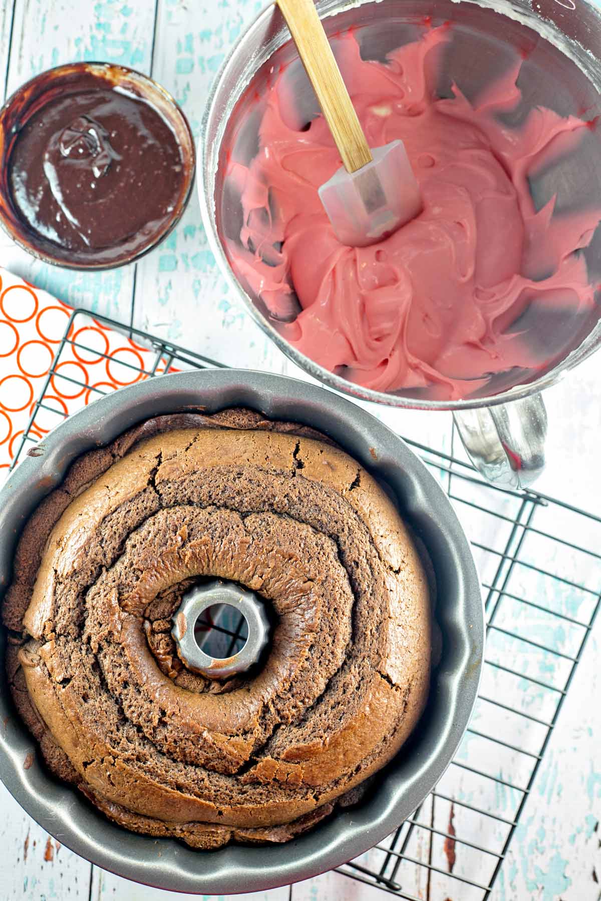 bundt cake still in the pan next to a bowl of pink cream cheese frosting.