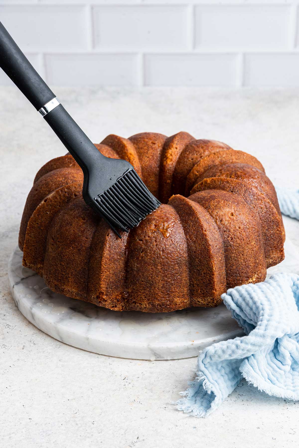 brushing a bundt cake with lemon simple syrup.