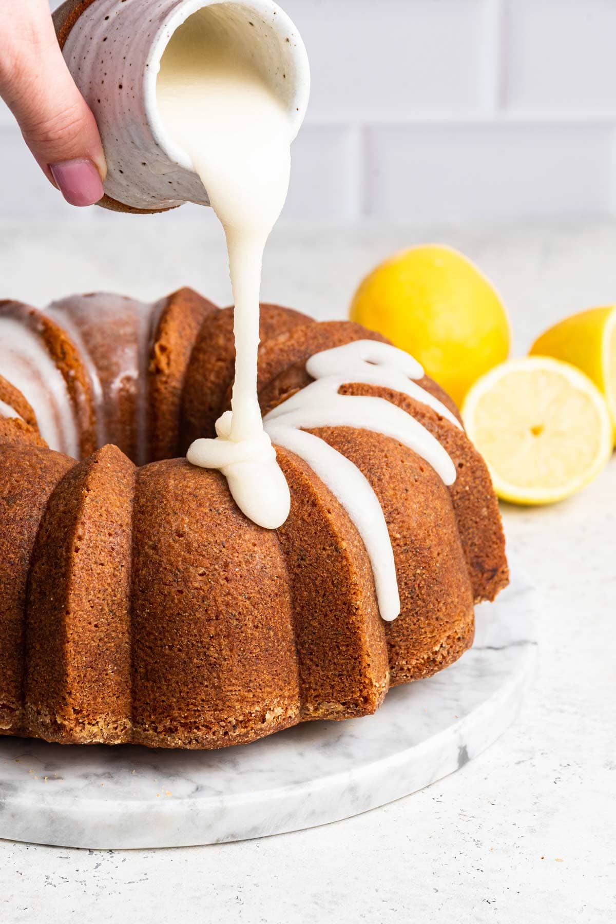 pouring a thick lemon glaze over a lemon pound cake.