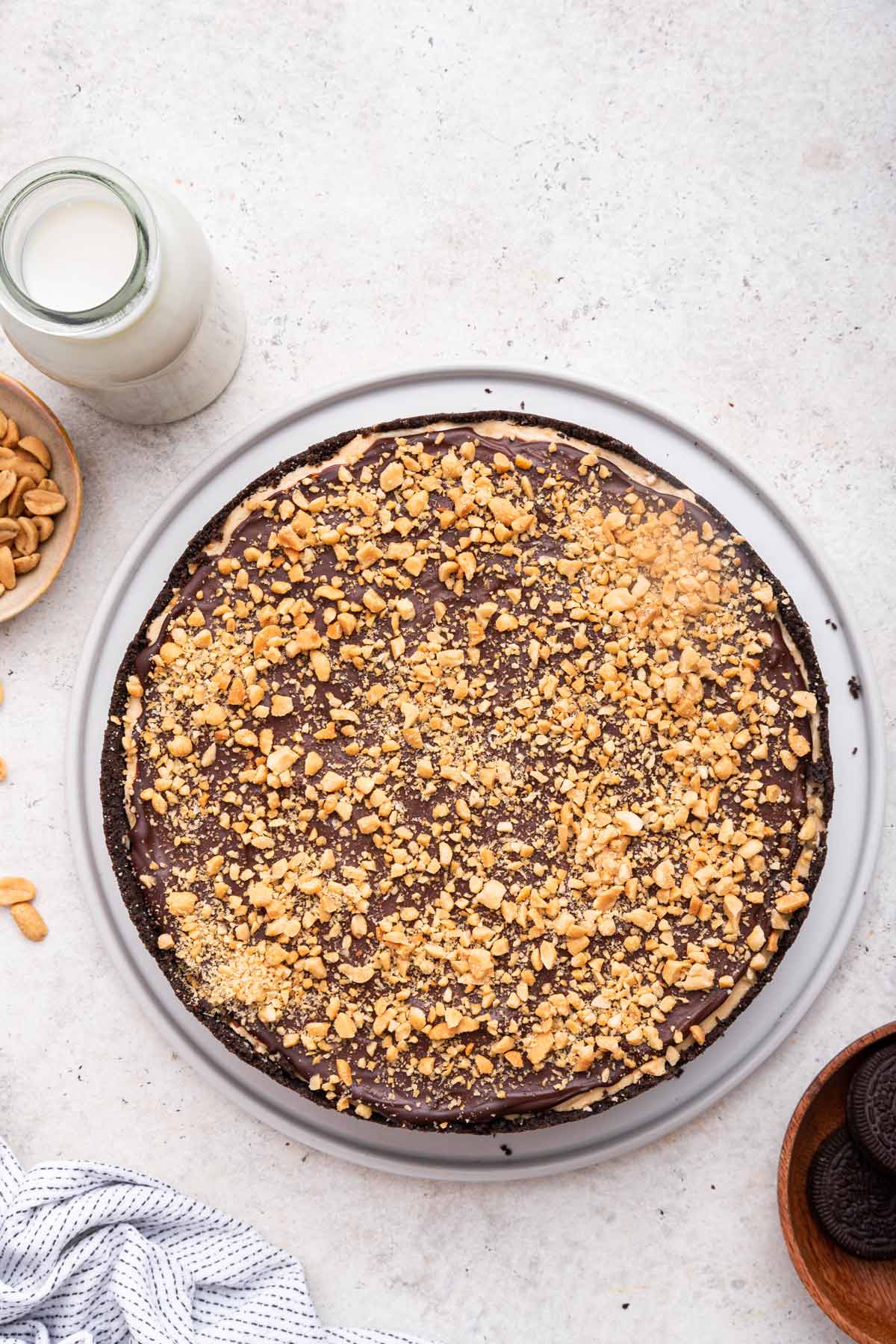 overhead view of a no bake peanut butter cheesecake with an oreo crust covered in ganache and chopped peanuts.