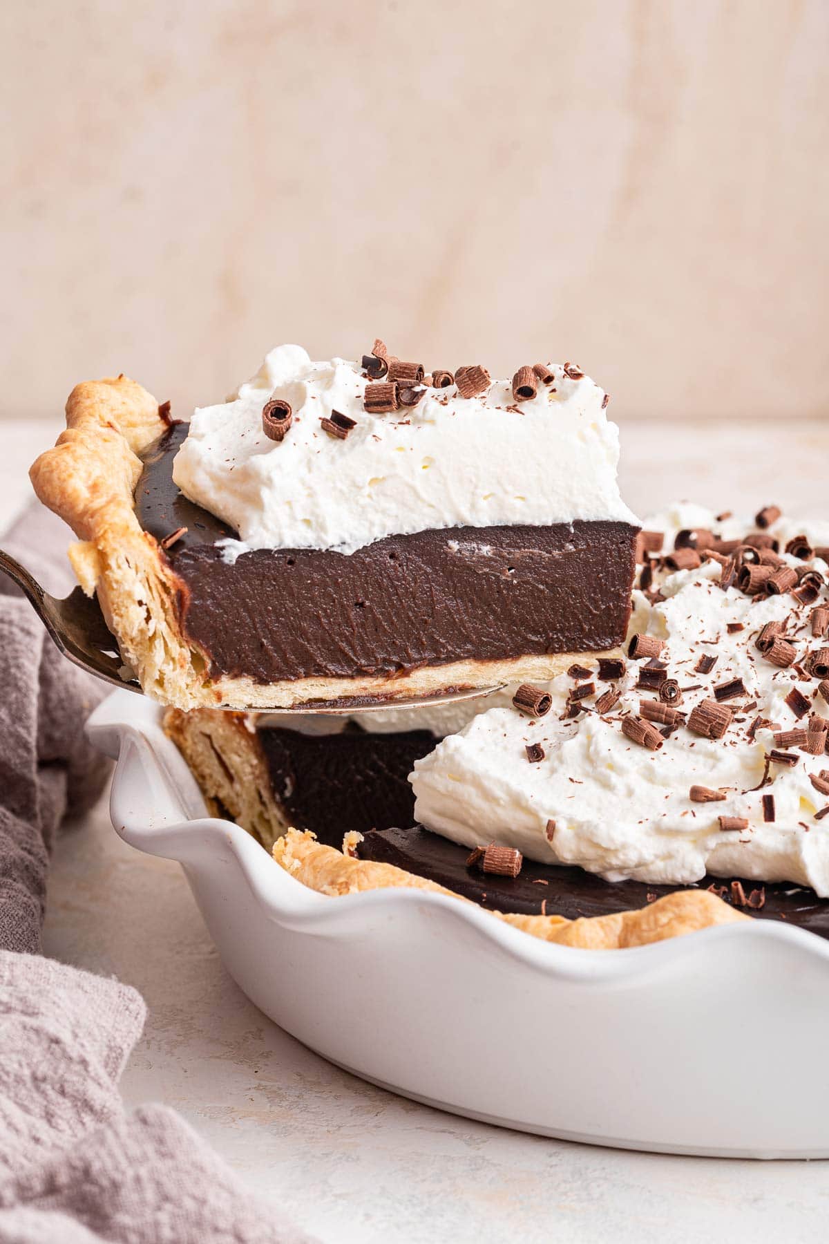 spatula lifting a thick slice of chocolate cream pie out of a pie dish.