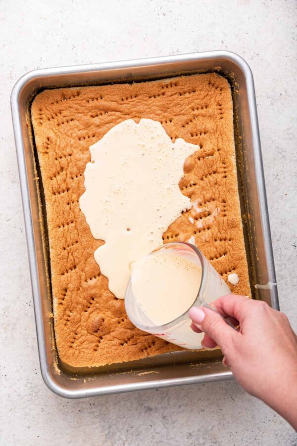 pouring milk from a measuring cup over the surface of a sponge cake.