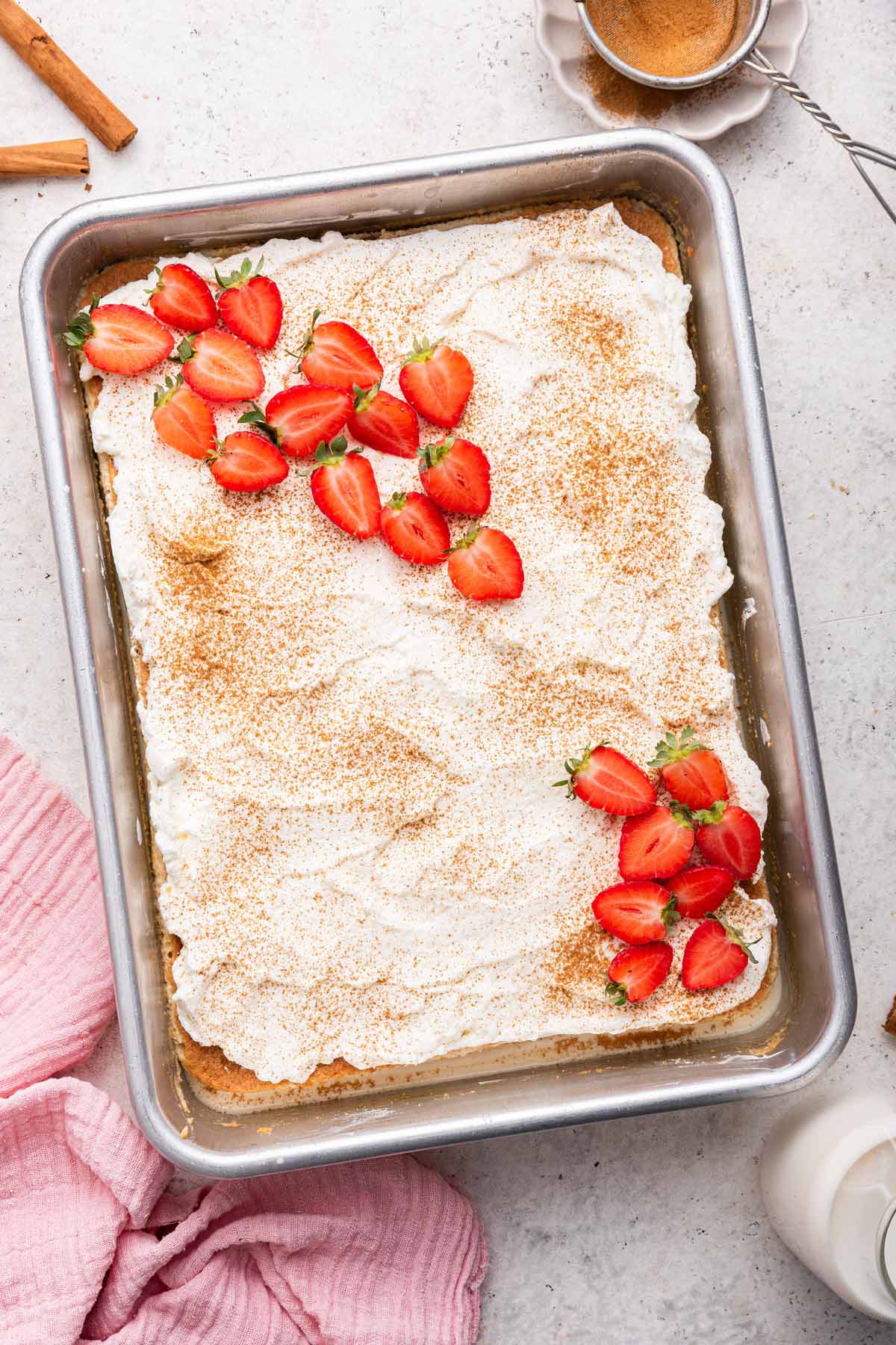 overhead view of a tres leches cake covered in whipped cream and sliced strawberries.