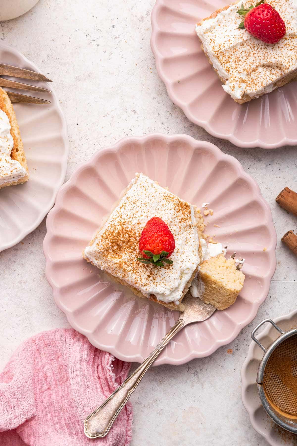 two slices of tres leches cake with sliced strawberries next to cinnamon sticks.