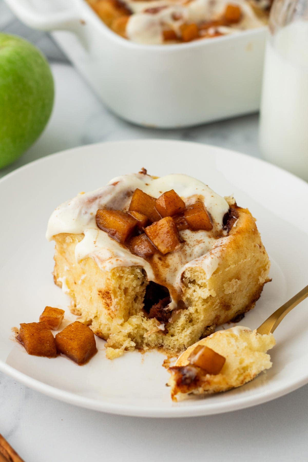 cinnamon roll covered with cooked apples on a plate with one forkful removed.