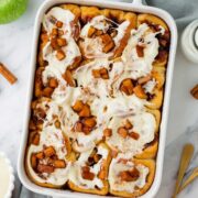pan of freshly baked cinnamon rolls covered with frosting and spiced apples.
