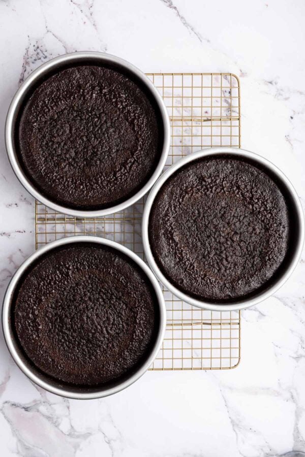three freshly baked layers of chocolate cake still in the cake pans.