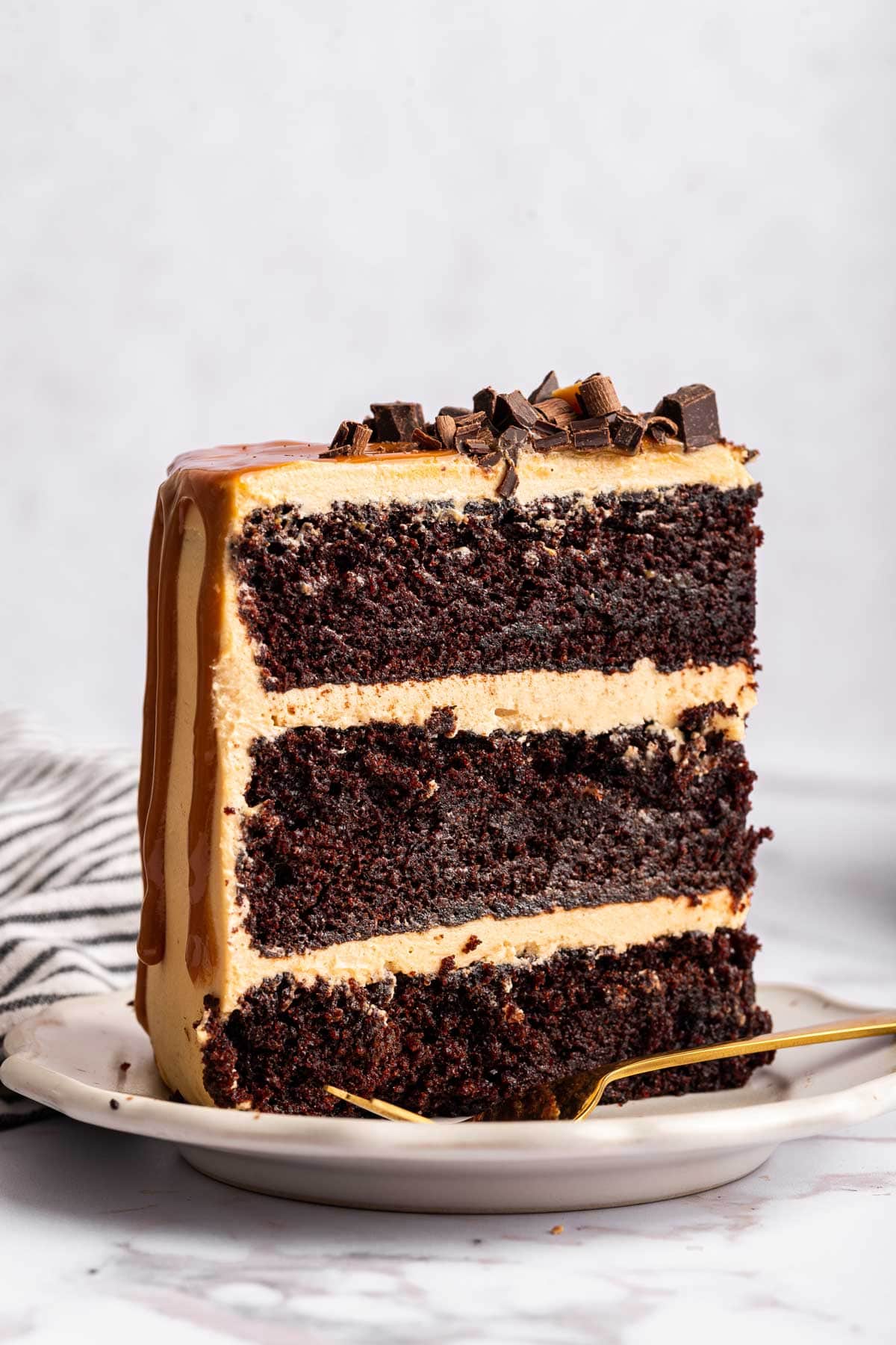 slice of three layer chocolate cake standing upright on a dessert plate.