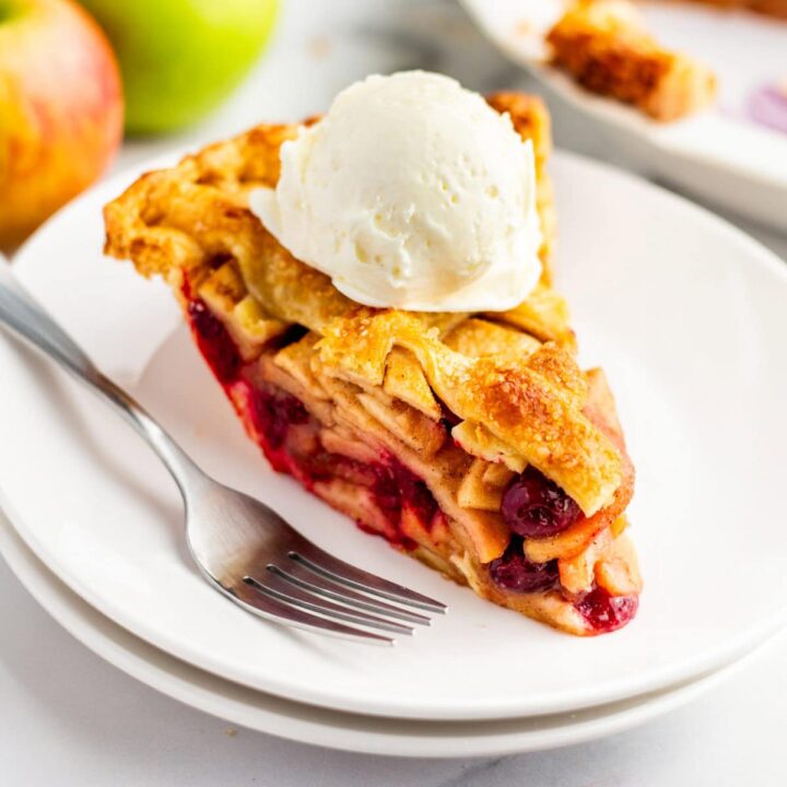side view of a slice of apple cranberry pie with a scoop of ice cream on top.