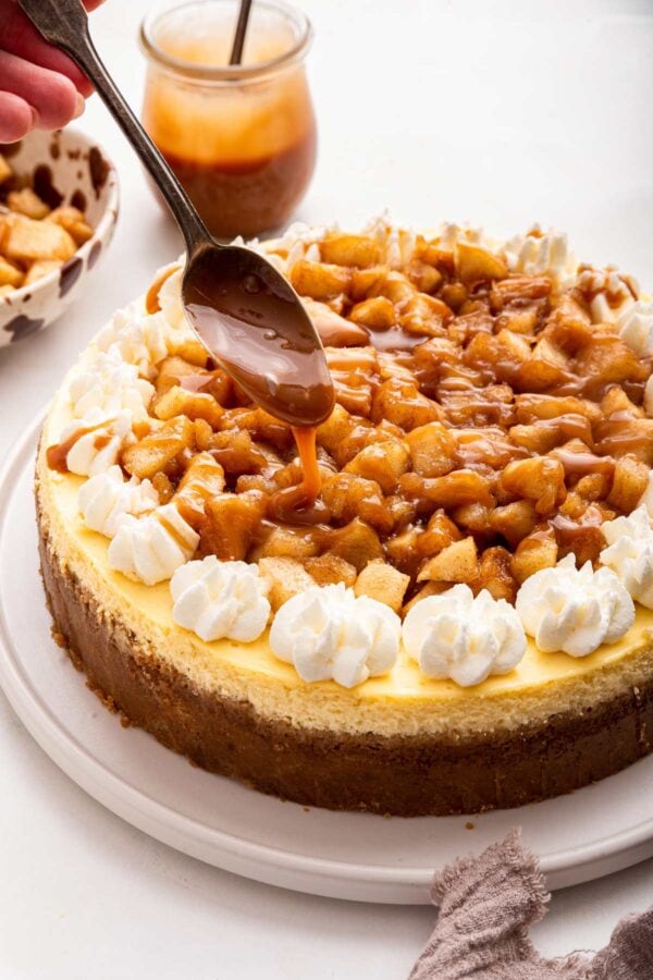 spooning caramel sauce on top of an apple cheesecake.