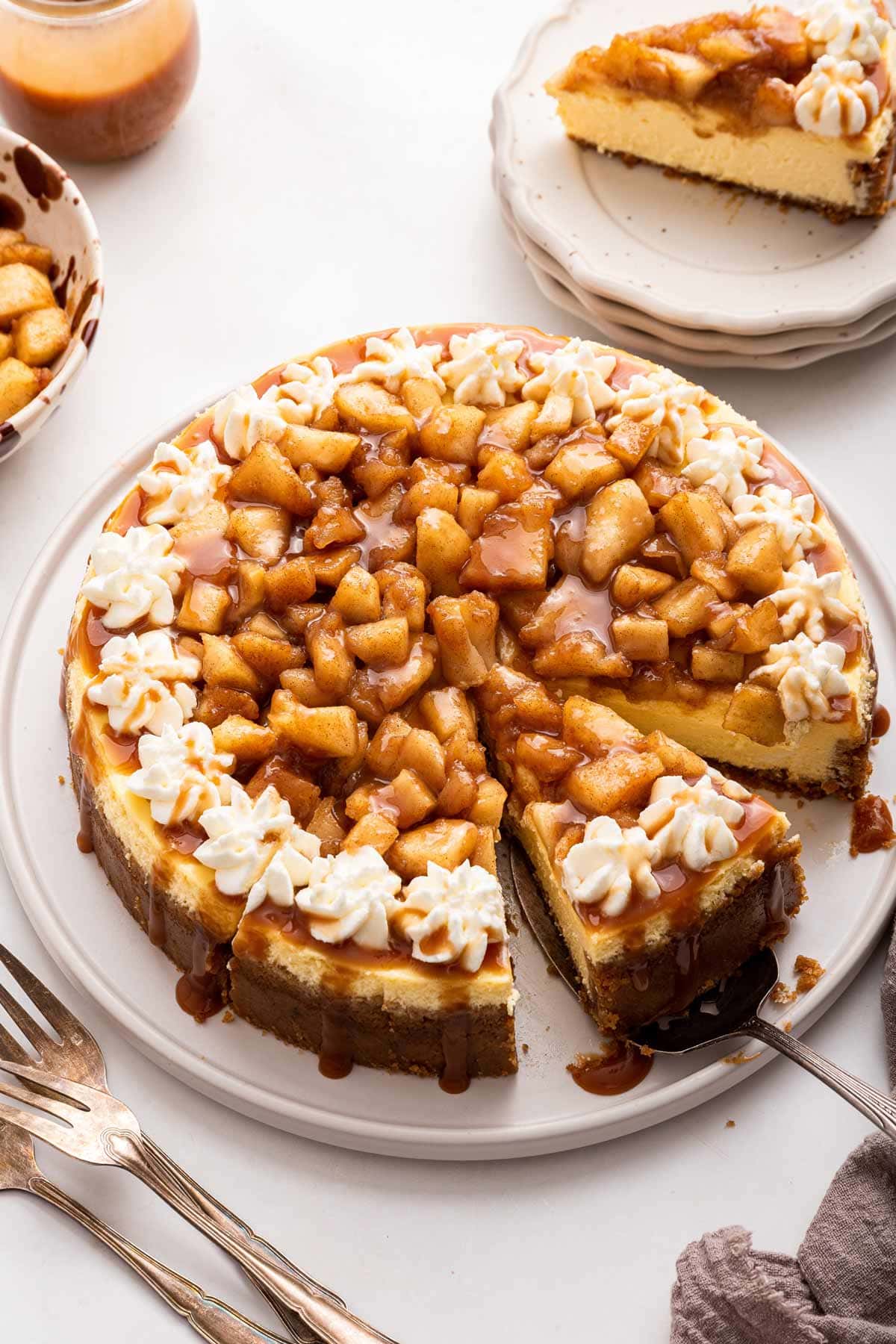cheesecake covered in cooked apples and caramel sauce with one slice removed.