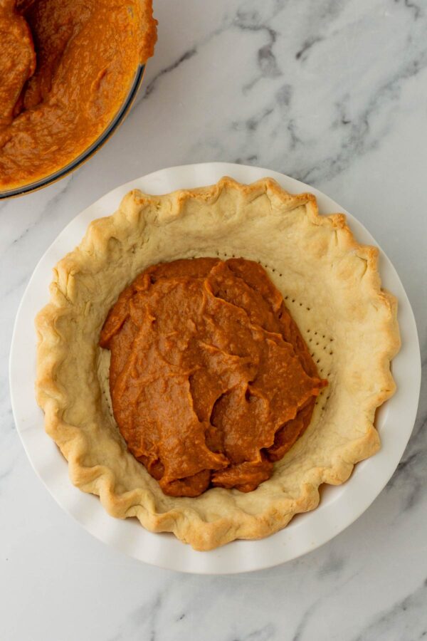 scooping sweet potato pie filling into a par-baked pie crust. 