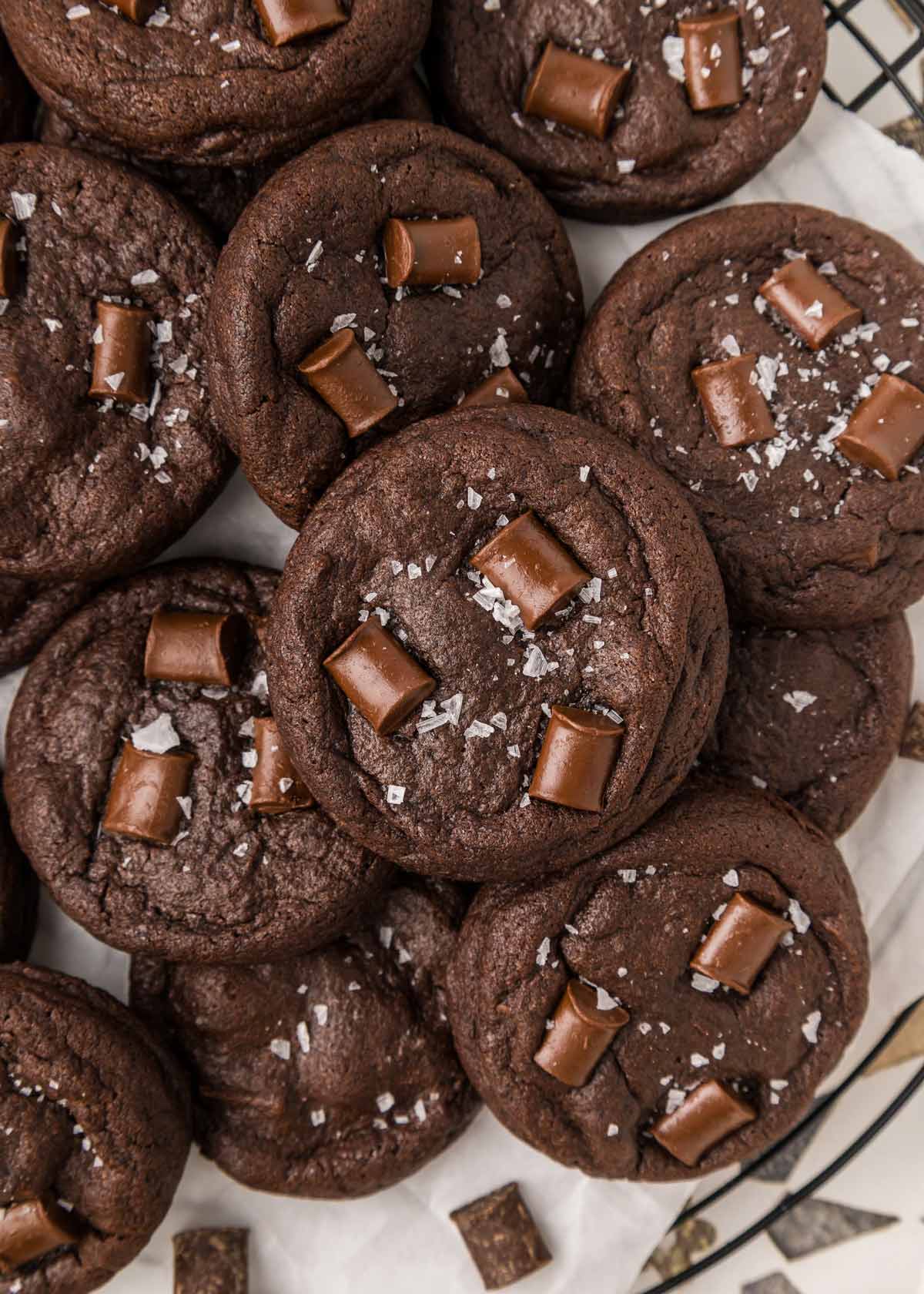 pile of dark chocolate cookies with chocolate chunks covered with flaky sea salt.