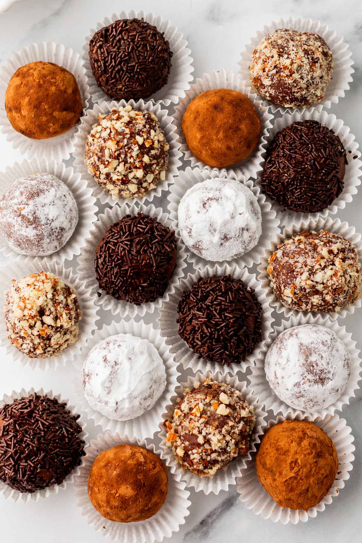 overhead view of rum balls rolled in powdered sugar, cocoa powder, nuts, and sprinkles.