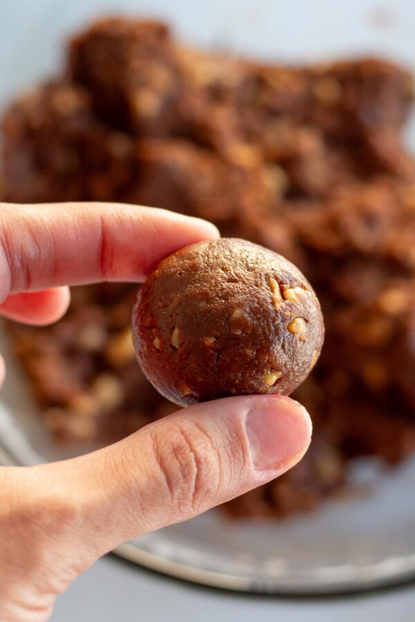 two fingers holding up a rolled bourbon ball before coating it.